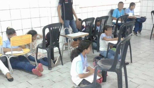 Por falta de carteiras, alunos sentam no chão.
